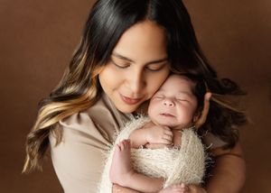 A tender moment captured in warm brown tones as a parent cradles their sleeping newborn baby in a soft knit wrap.