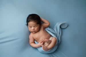 Sleeping newborn baby wearing light blue wrap photographed from multiple angles on blue background.