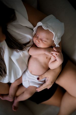 A sleeping newborn wearing a delicate white lace bonnet rests peacefully in white clothing.