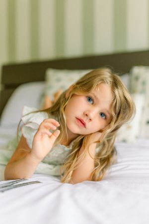 A series of four photos showing a young child with blonde hair lying in white bedding making playful expressions.