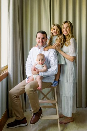 A family in white and beige clothing poses together against a curtained backdrop in three similar portrait shots.