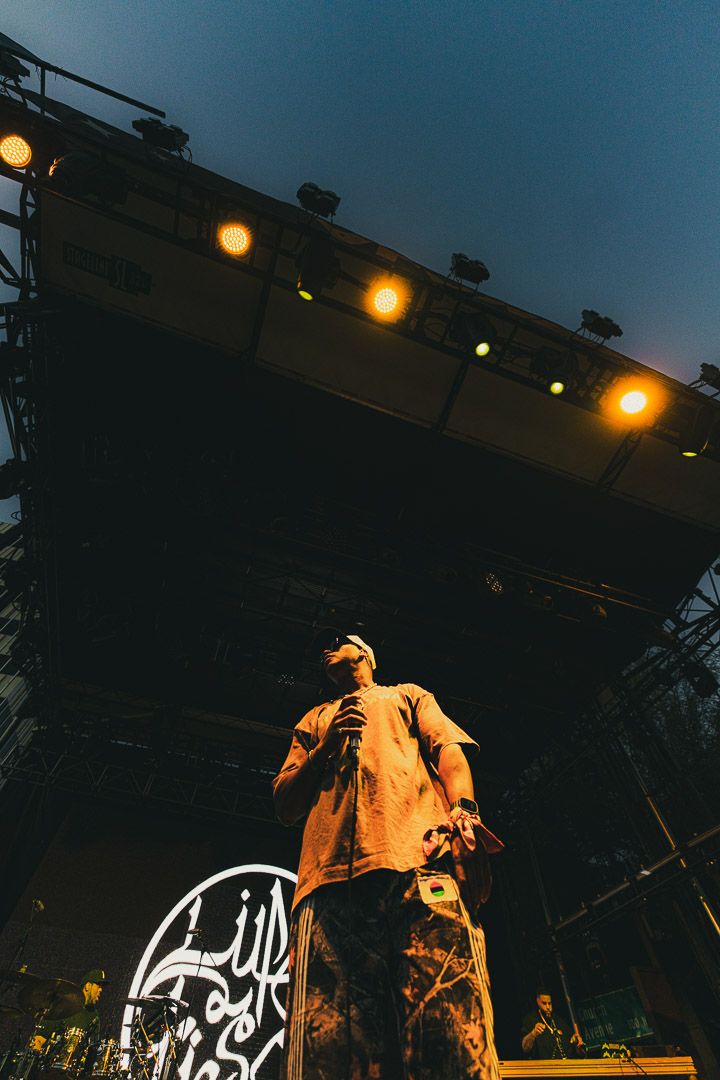 Silhouetted performers on a dimly lit outdoor concert stage with glowing lights in the background.