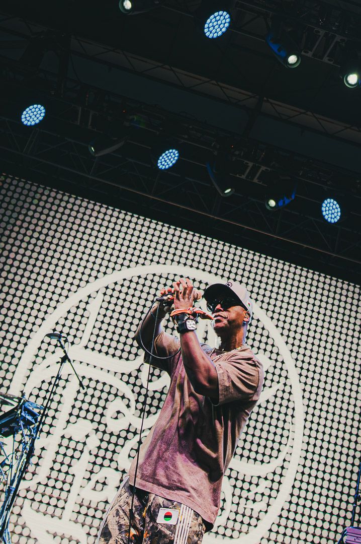 A performer sings on stage with blue spotlights overhead and a geometric patterned backdrop during a concert.