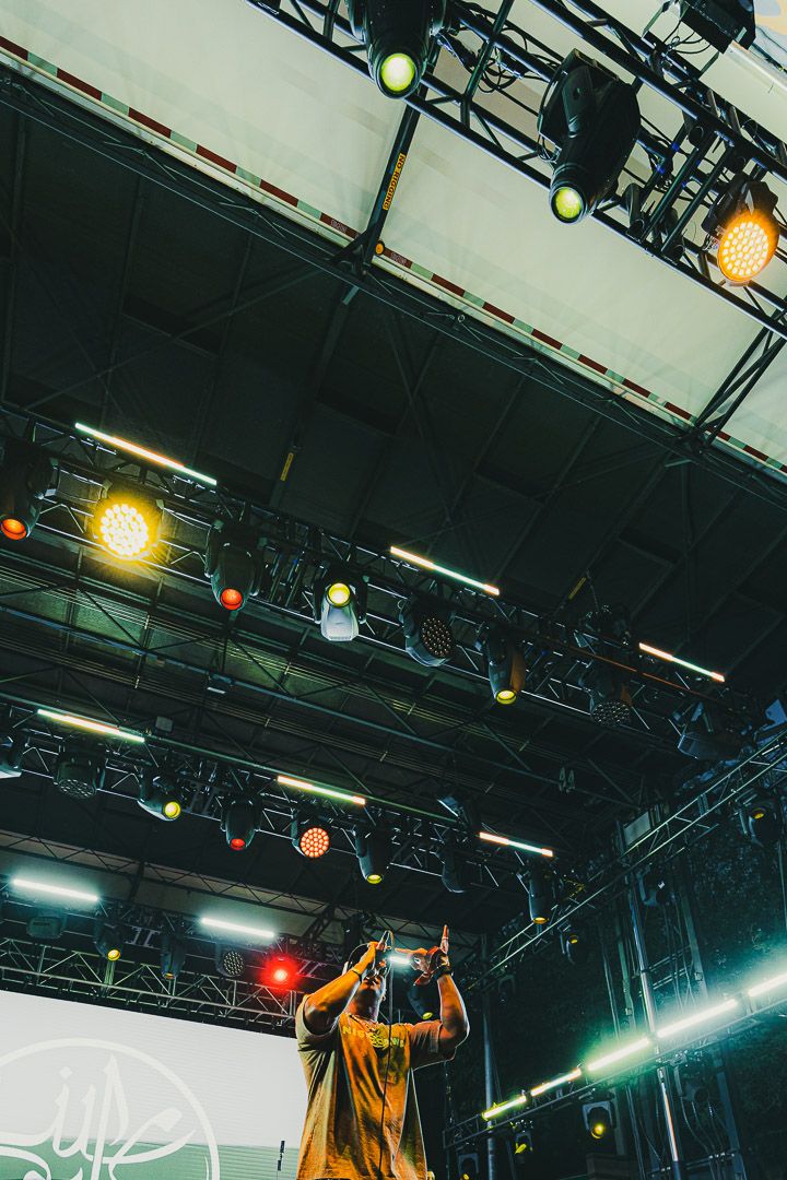 Concert venue with stage lighting rigs and a performer in yellow clothing singing under dramatic spotlights.