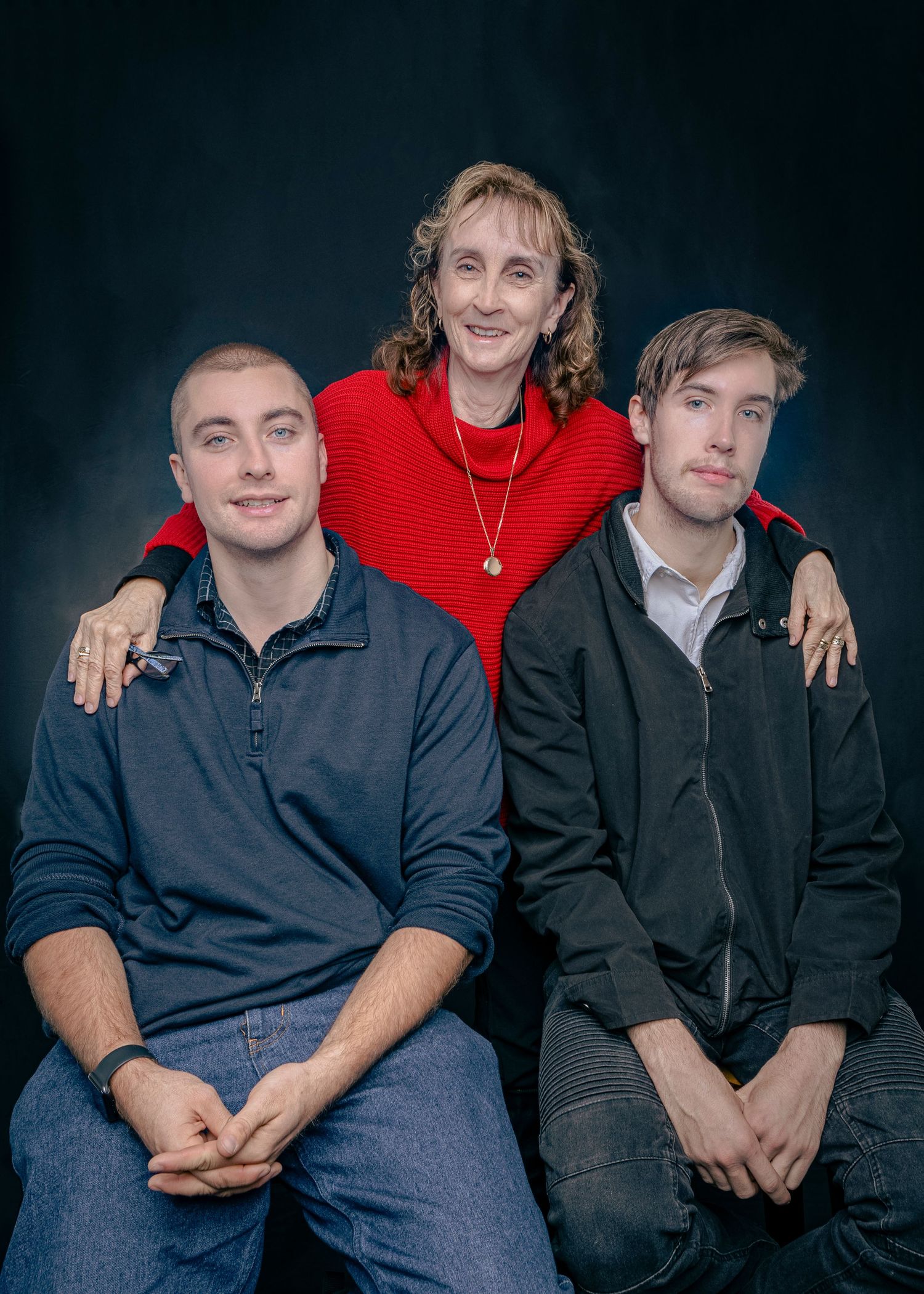 Three people in dark clothing sit together against a dark background in a casual group photo.