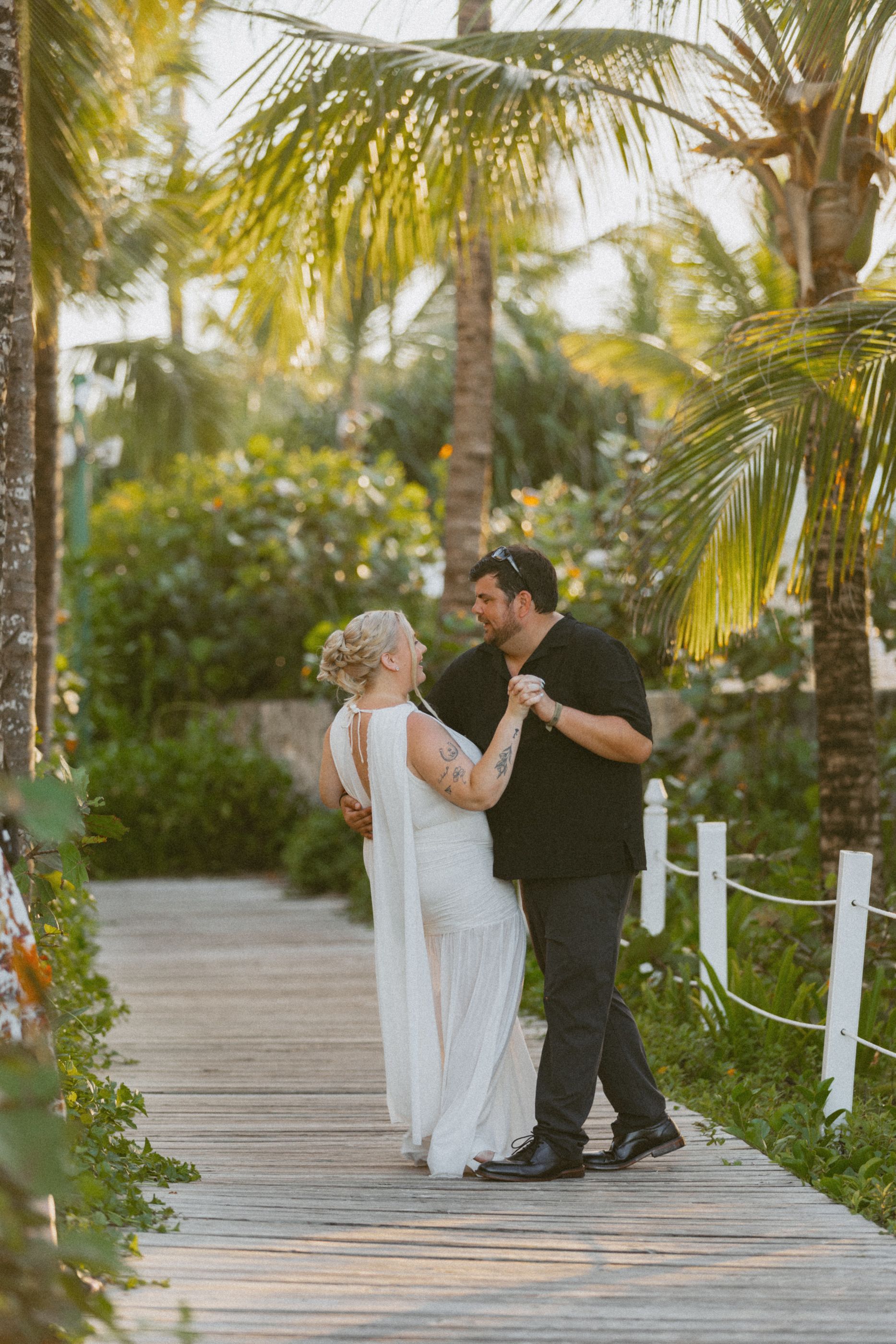 Couple dancing on wooden boardwalk surrounded by tropical palm trees.