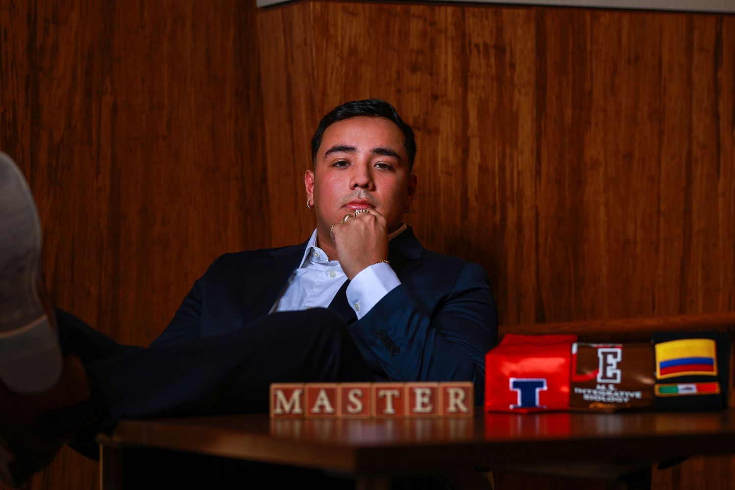A person in a suit sits at a wooden table in what appears to be a courtroom or formal meeting space.