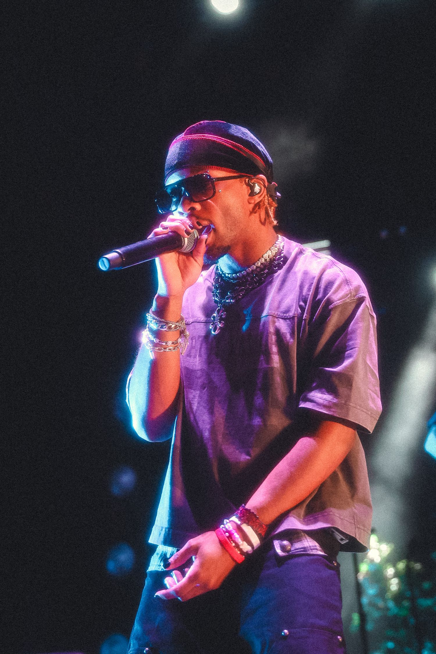 Concert performer in a baseball cap singing into a microphone on stage with dramatic purple lighting effects.