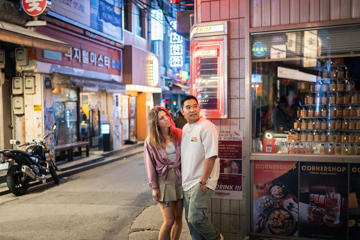 Colorful illuminated storefronts and signs line a narrow alley in an Asian night market.