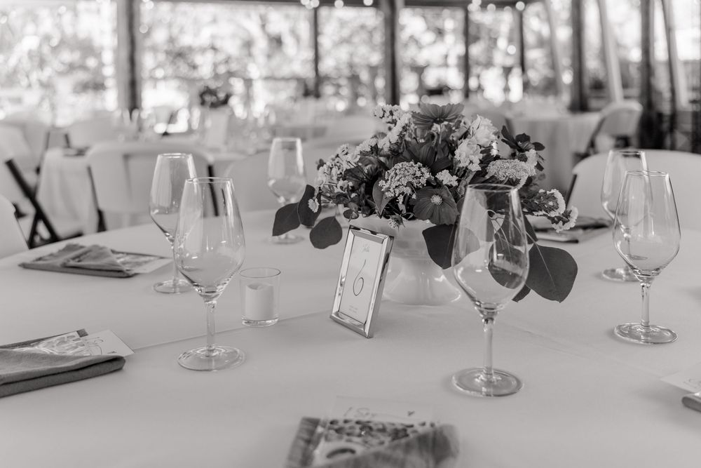 Elegant black and white photo of a formal table setting with wine glasses and floral centerpieces at a wedding reception.