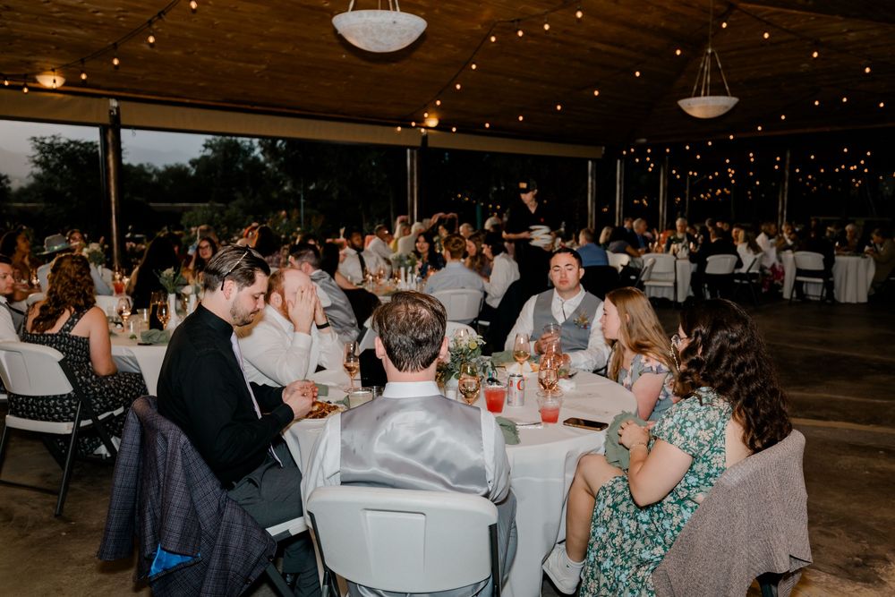 A festive wedding reception in a rustic barn venue with string lights and guests seated at long tables.