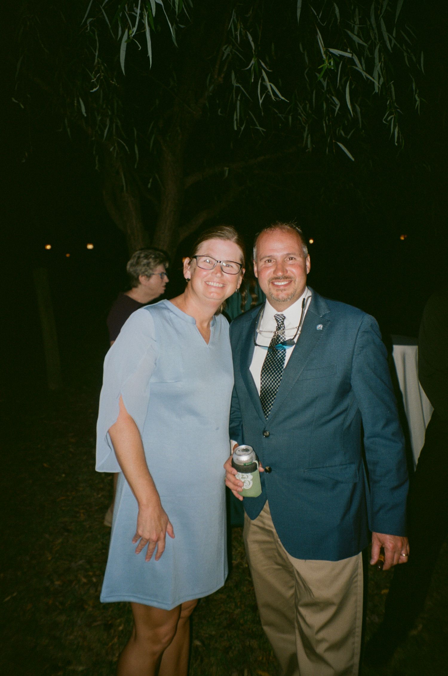 A group of people in formal attire gather together at an evening outdoor event.