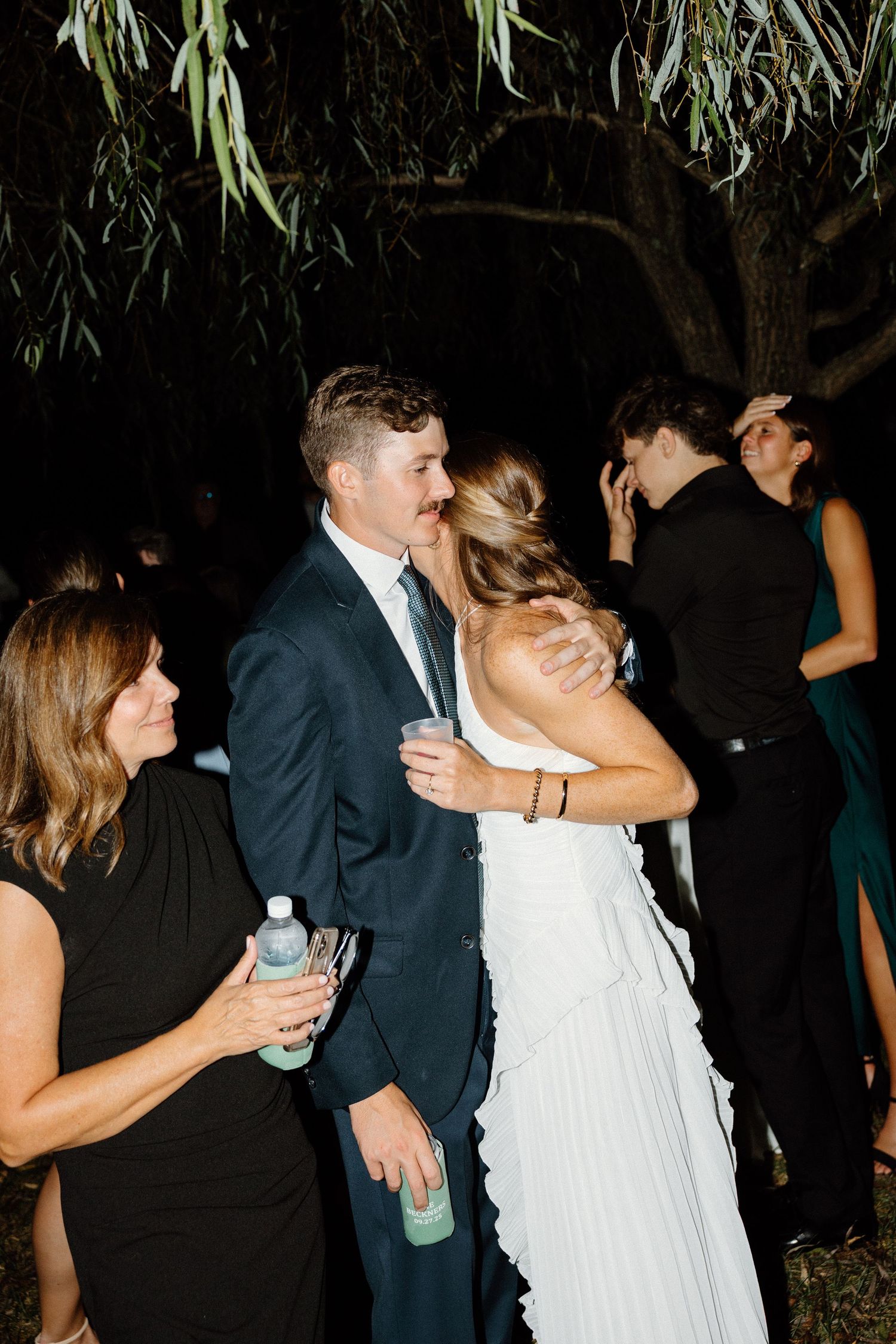 Couples dancing together at an outdoor evening wedding reception under hanging trees and string lights.