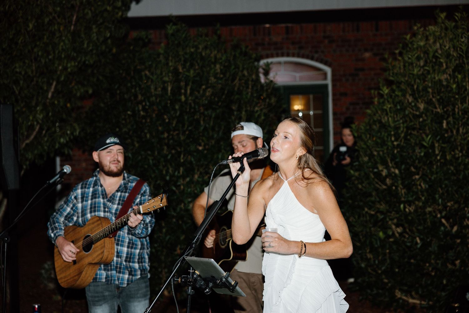 Musicians perform on stage at an outdoor venue with acoustic guitars and microphones during a live concert.