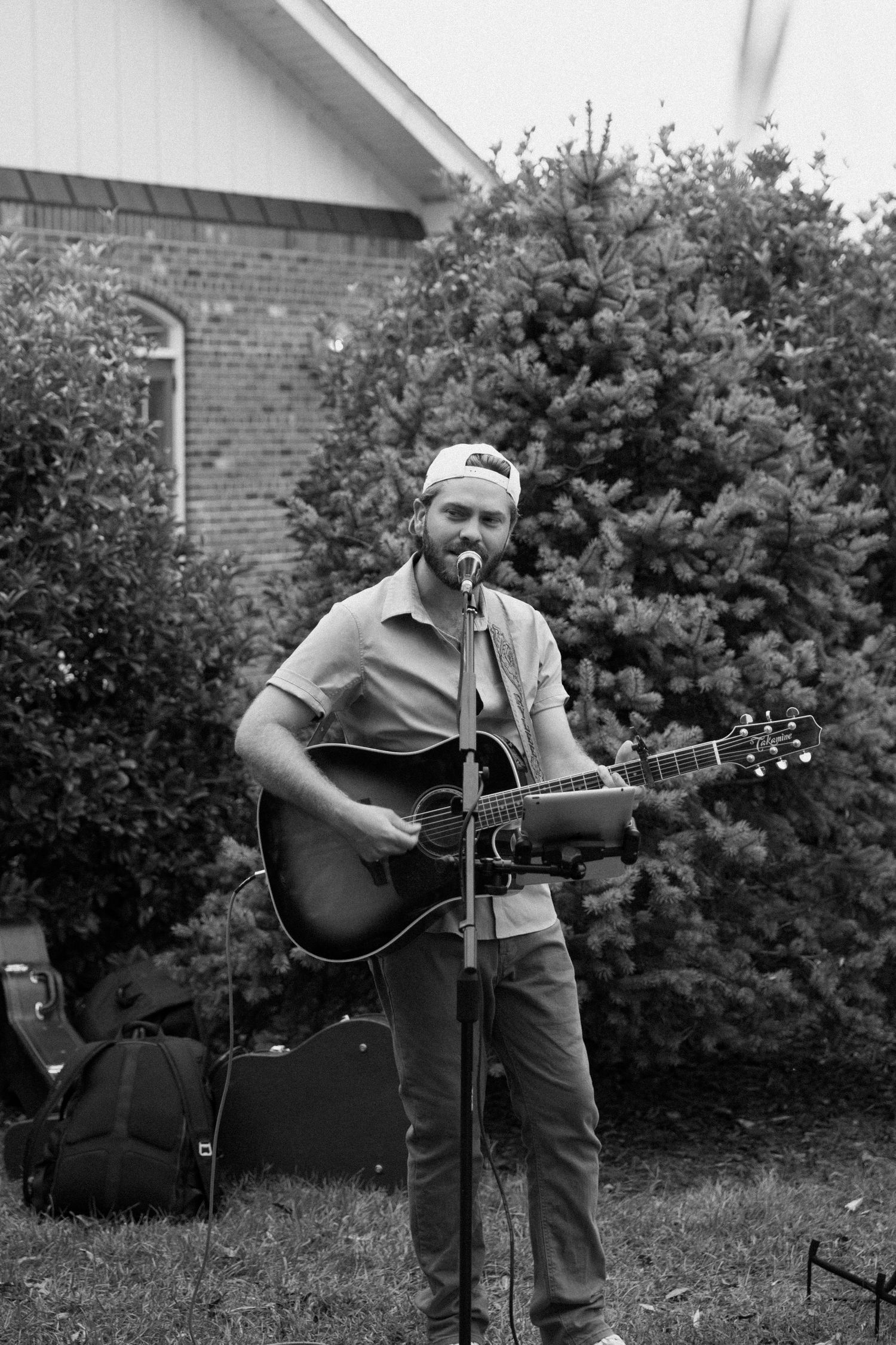A series of black and white photos showing someone playing an acoustic guitar outdoors next to a brick building.