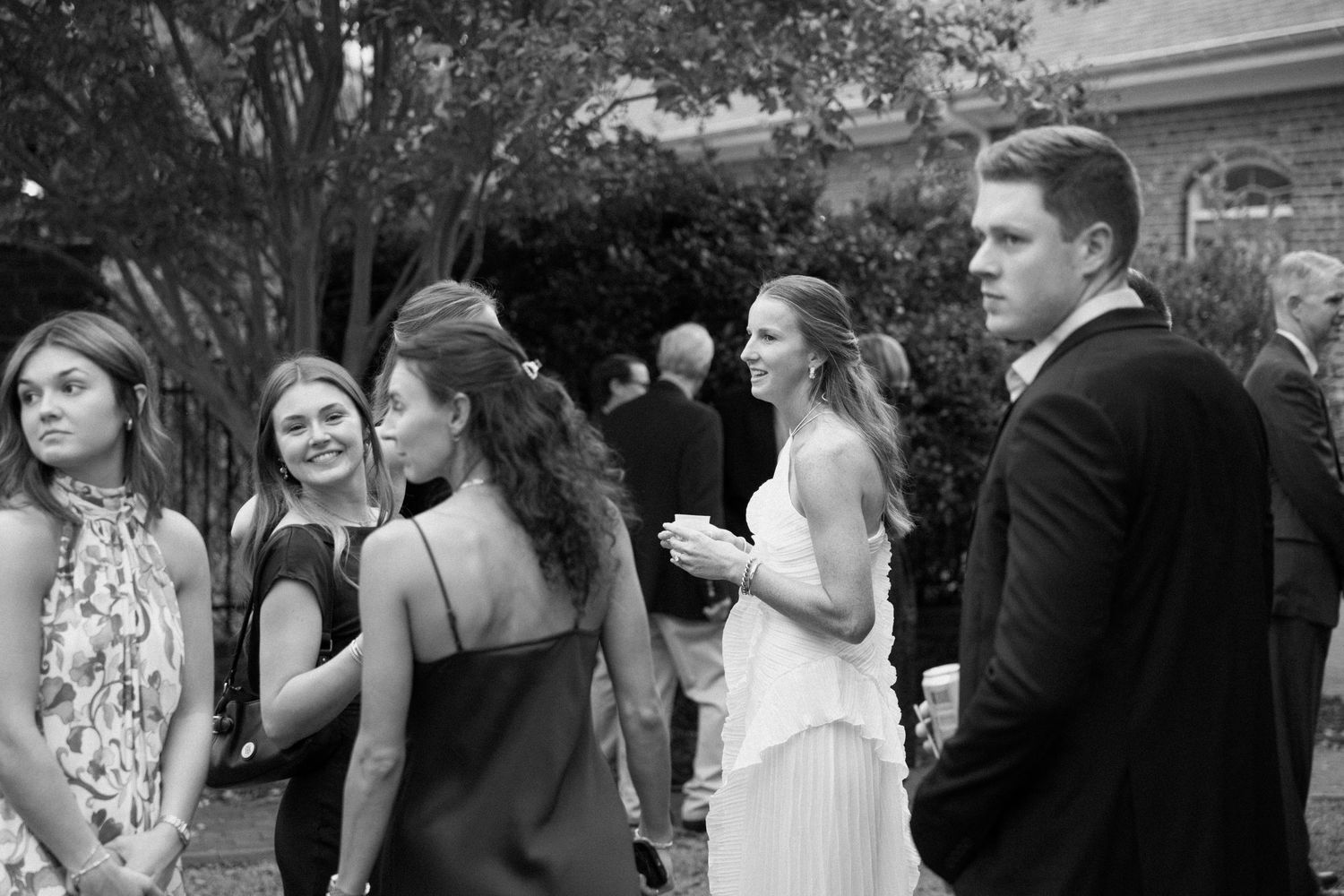 A black and white photograph showing a group of wedding guests celebrating at an outdoor reception.
