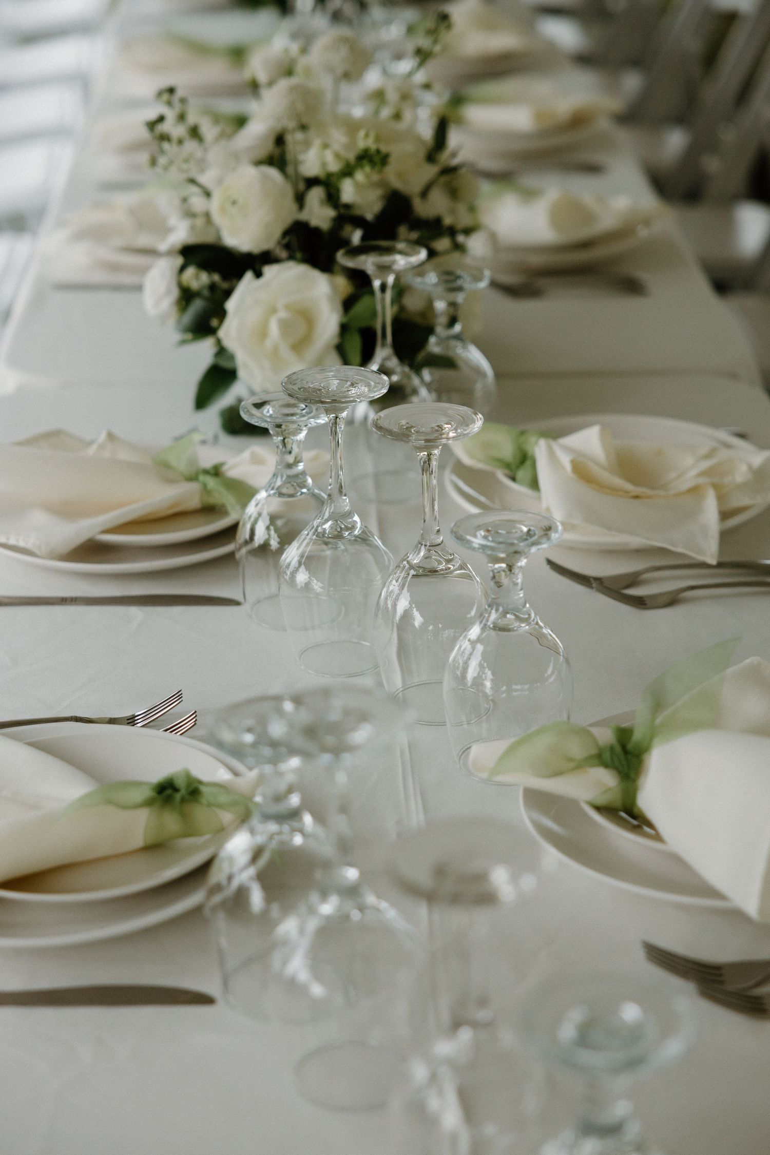 Elegant white table setting with crystal wine glasses and white floral centerpieces for a formal dining event.