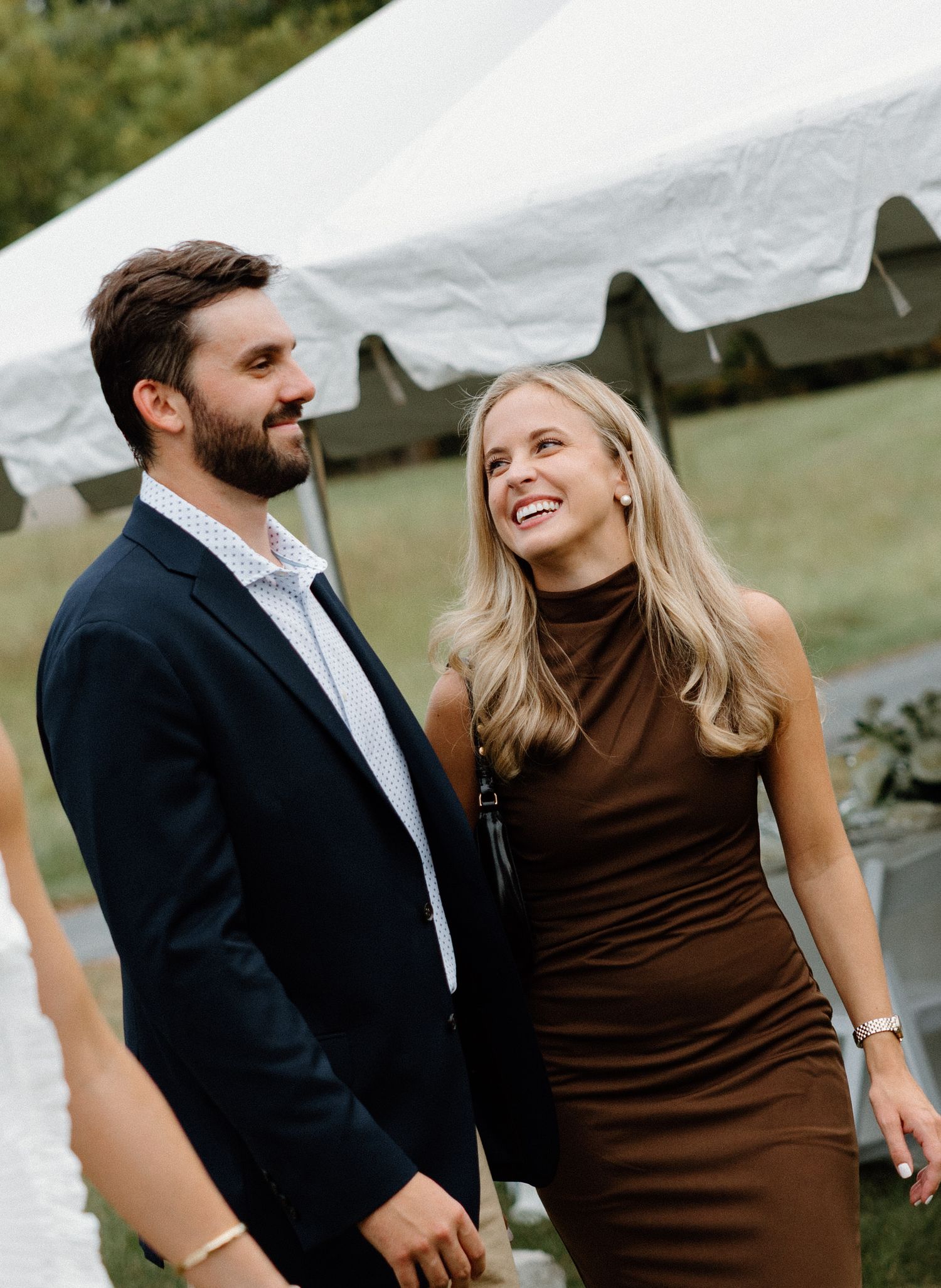 A couple shares a joyful moment together outdoors, with the woman wearing a brown dress and the man in a dark suit.