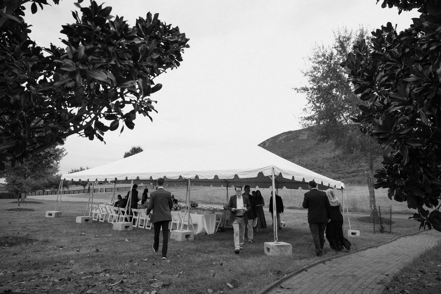 Vintage black and white photograph showing people gathered at a rural outdoor event with tents and wagons visible.