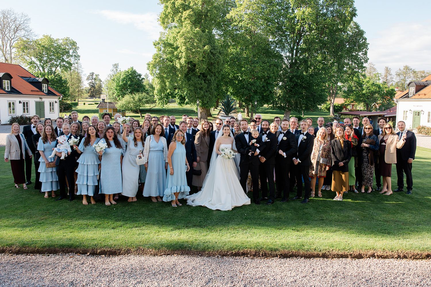 Wedding party poses outdoors for formal group photos on a sunny summer day at an elegant venue.