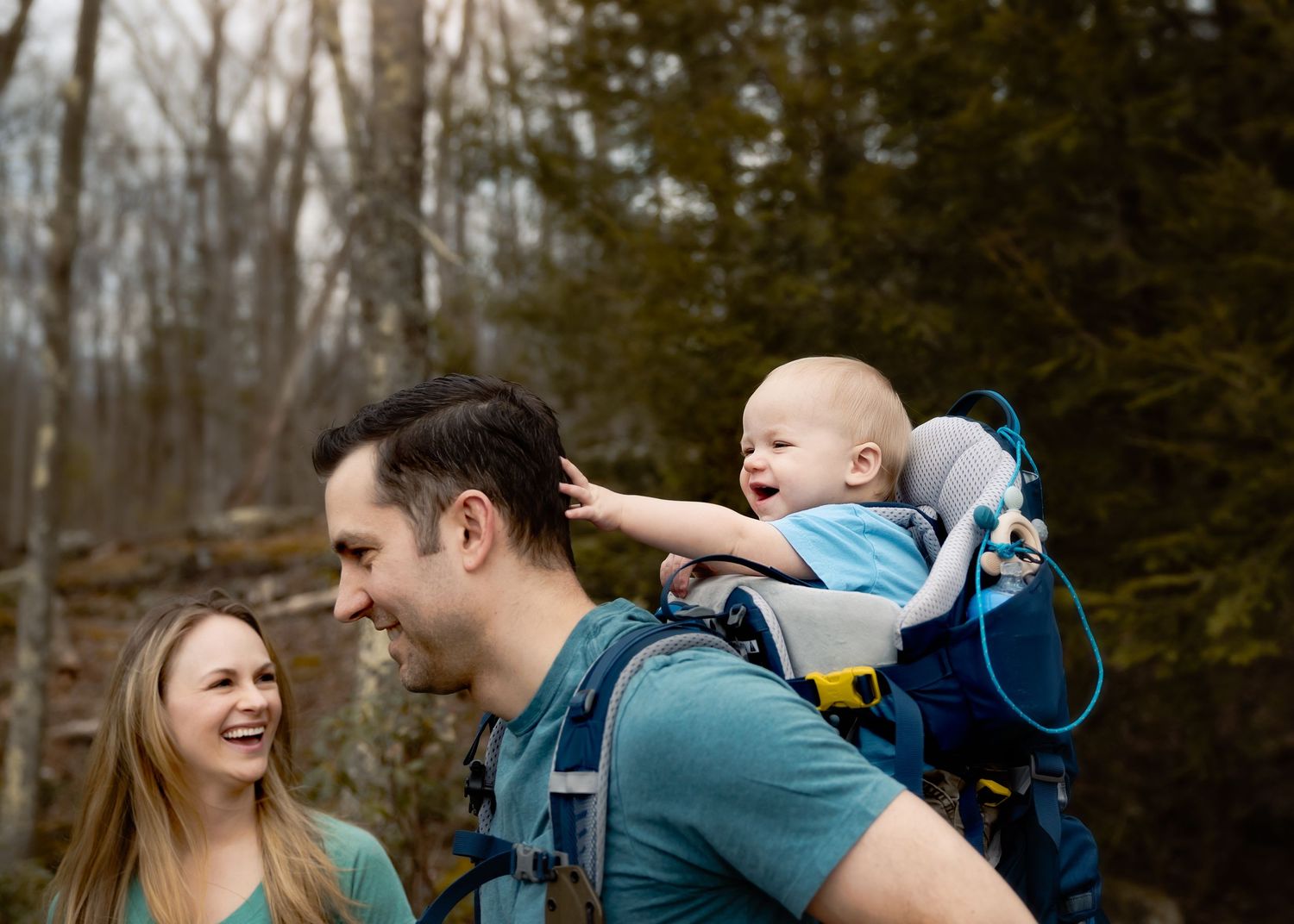 A couple laughs and embraces while hiking through a wooded trail on a winter day.