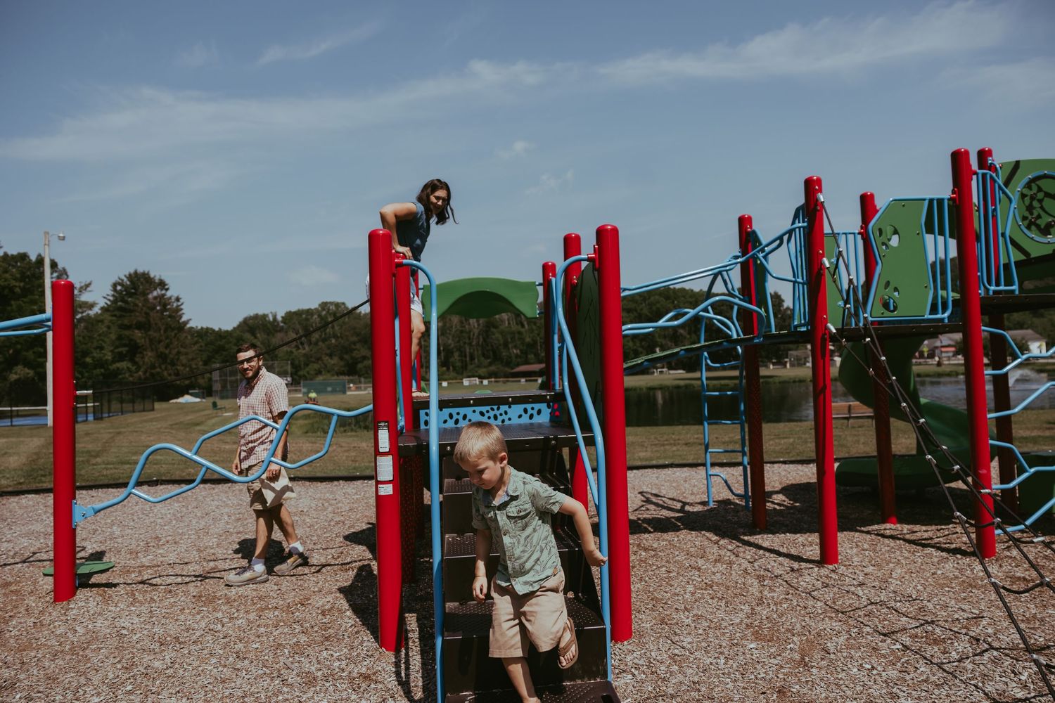 A colorful outdoor playground with red and blue poles arranged in a row along a gravel path.
