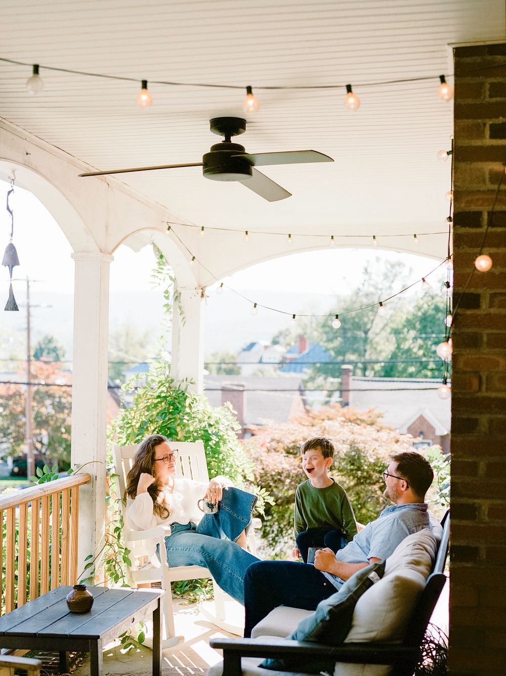 People relaxing on a covered porch with string lights and ceiling fans on a warm evening.