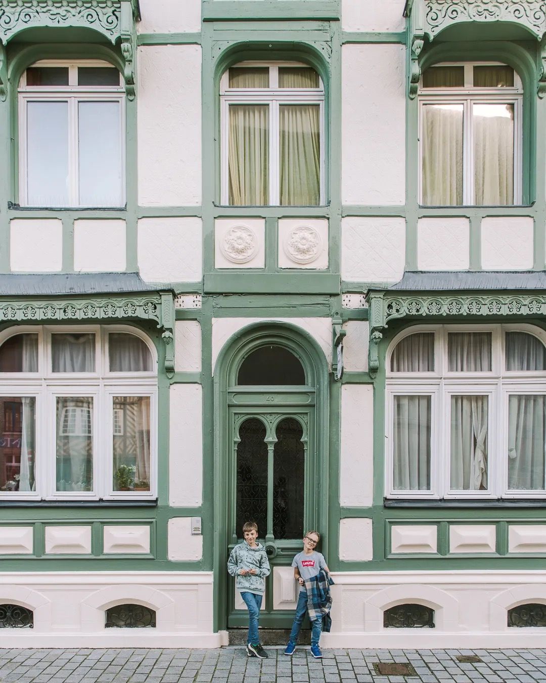 Family standing outside a green-and-white French townhouse with ornate windows.
