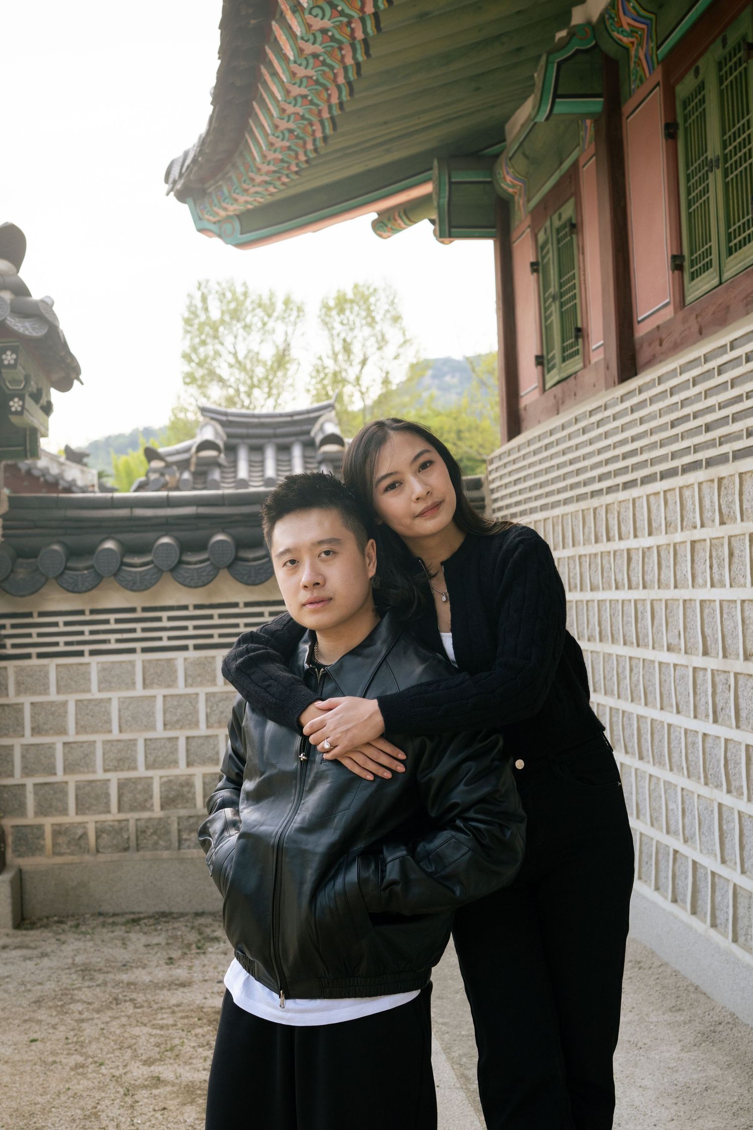 Two people in dark clothing embrace while standing in a traditional Korean palace corridor with ornate architecture.