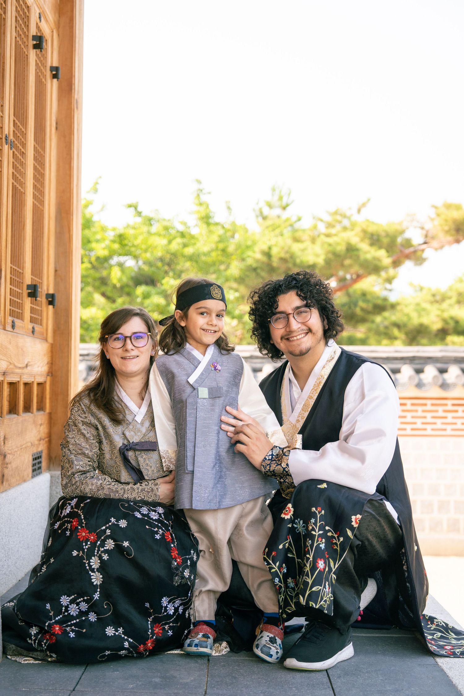 A group of friends in traditional Korean hanbok dresses sit together on a wooden porch during sunset.