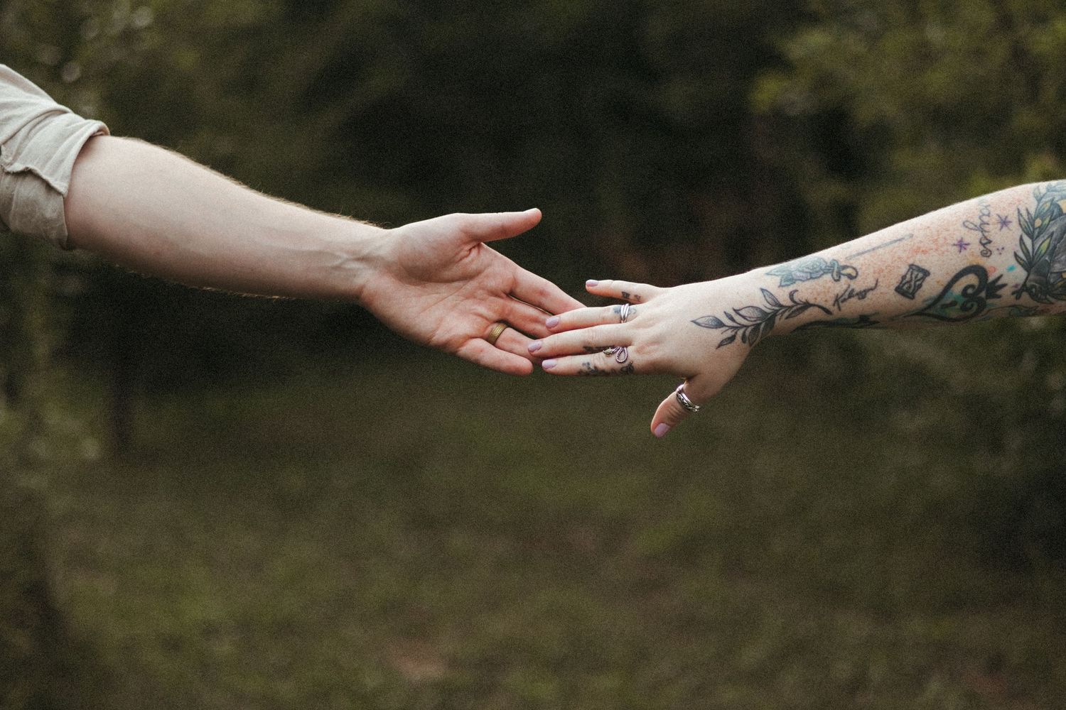 two hands lighting grazing each other, one has tattoos and rings