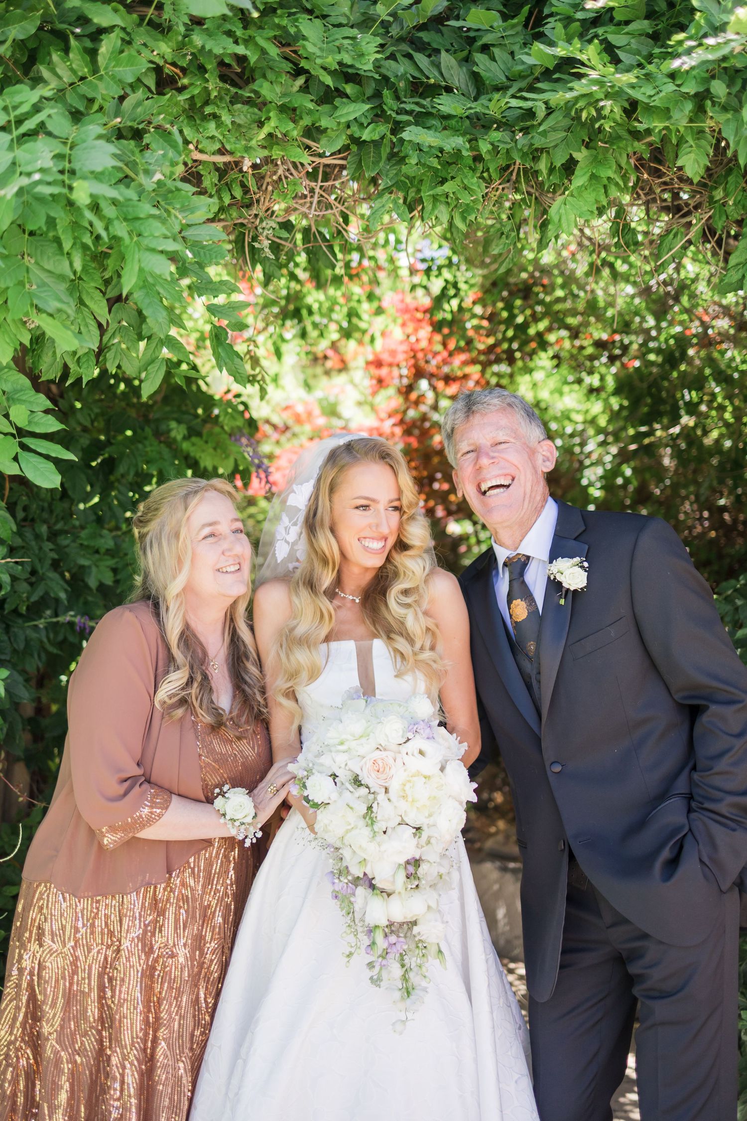 Wedding party in formal attire poses together outdoors with bouquets and floral arrangements.
