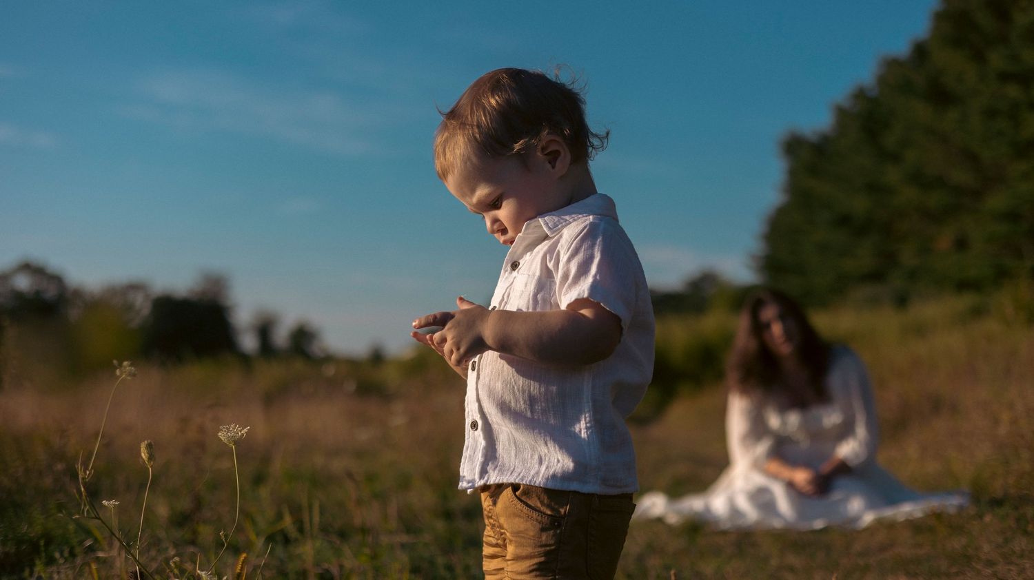 A person in a white shirt sits in a grassy field during golden hour sunset.