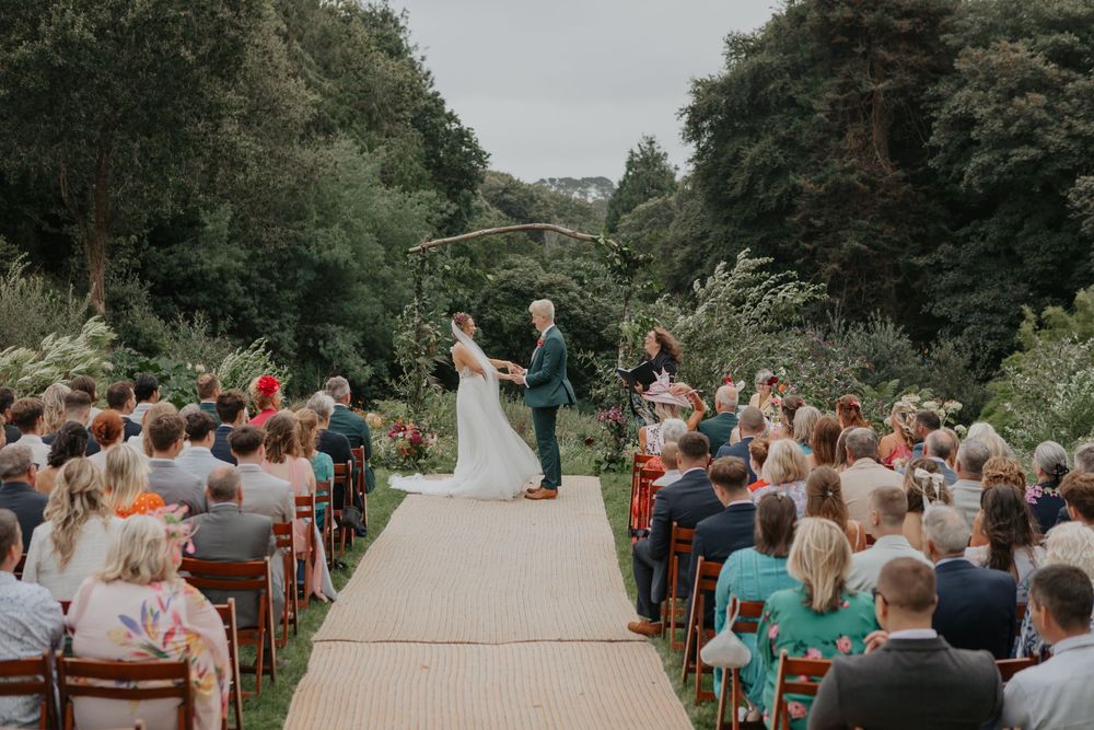 Bride and groom stand at altar under rustic arch during outdoor garden wedding ceremony.