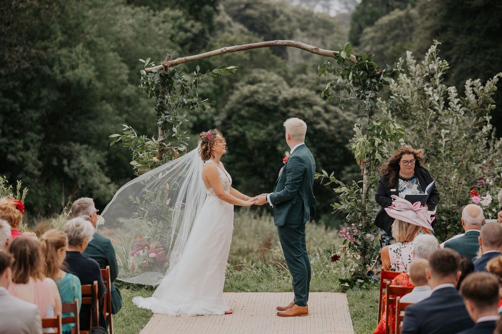 Bride and groom exchange vows under rustic branch arch at outdoor garden wedding.