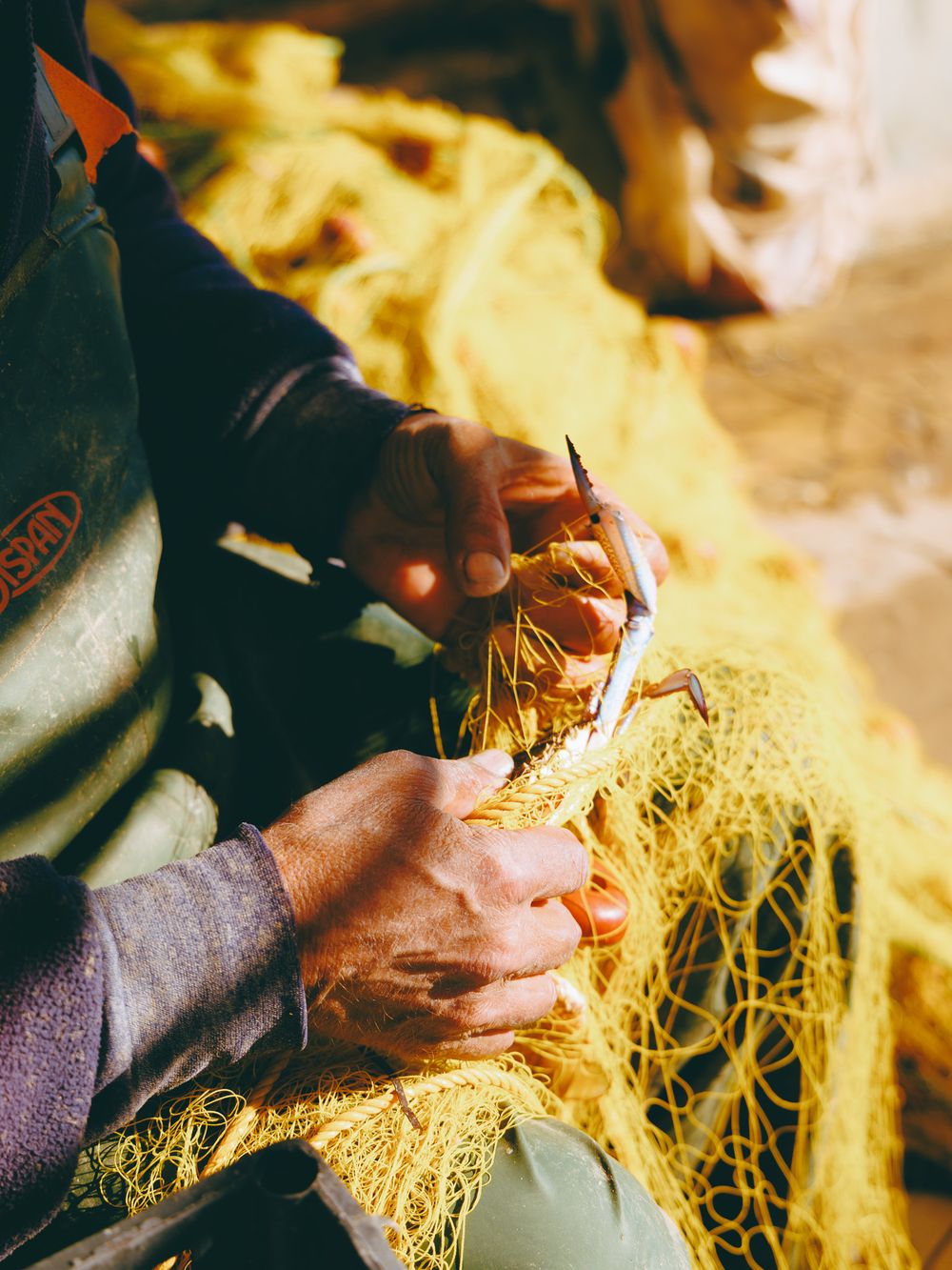 Close-up of hands working with yellow fishing nets on a traditional boat in Crete, documentary coastal life detail.