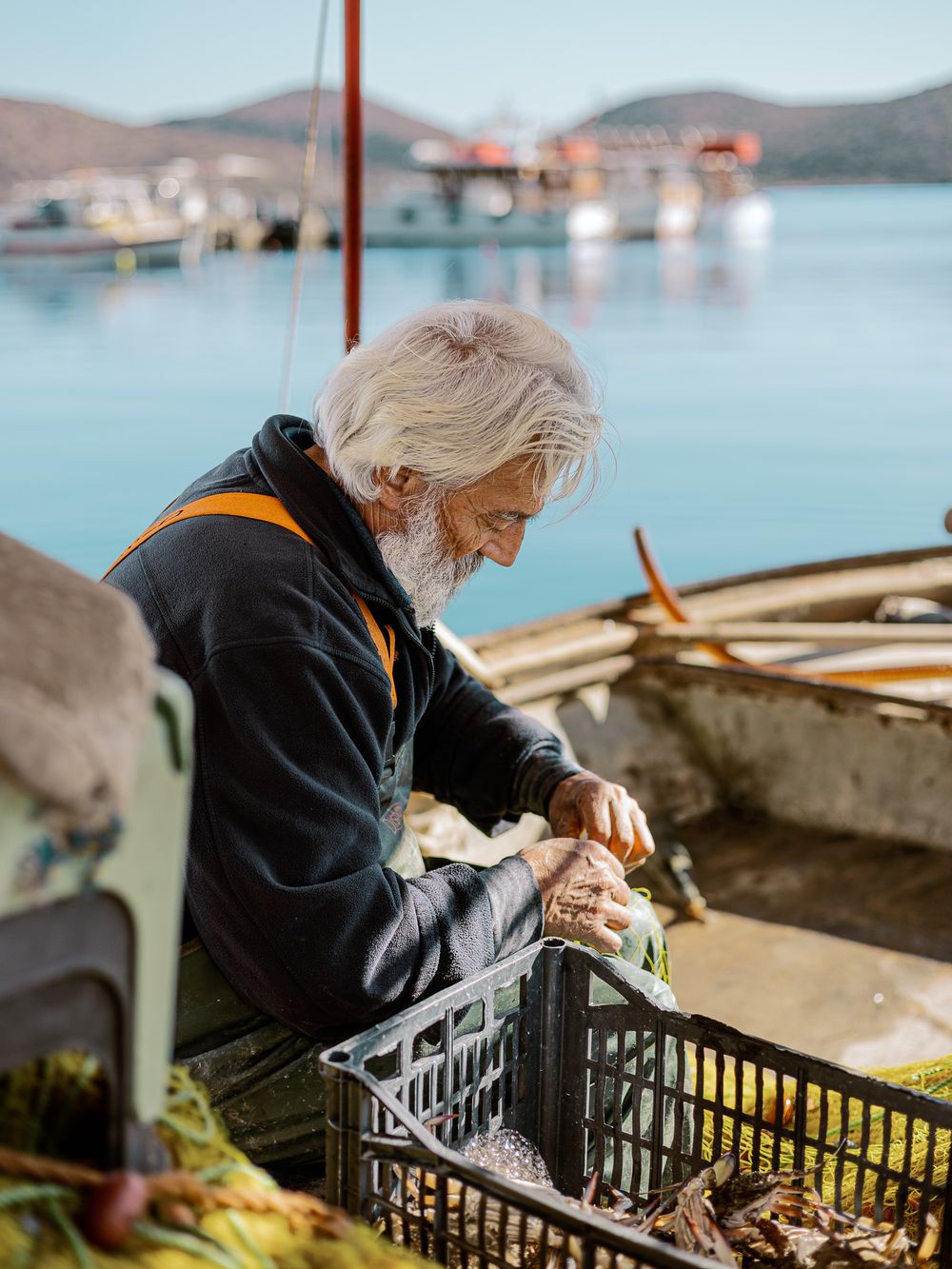 Fisherman in Elounda, Crete preparing his catch on a small boat, calm morning light and quiet harbour in the background.