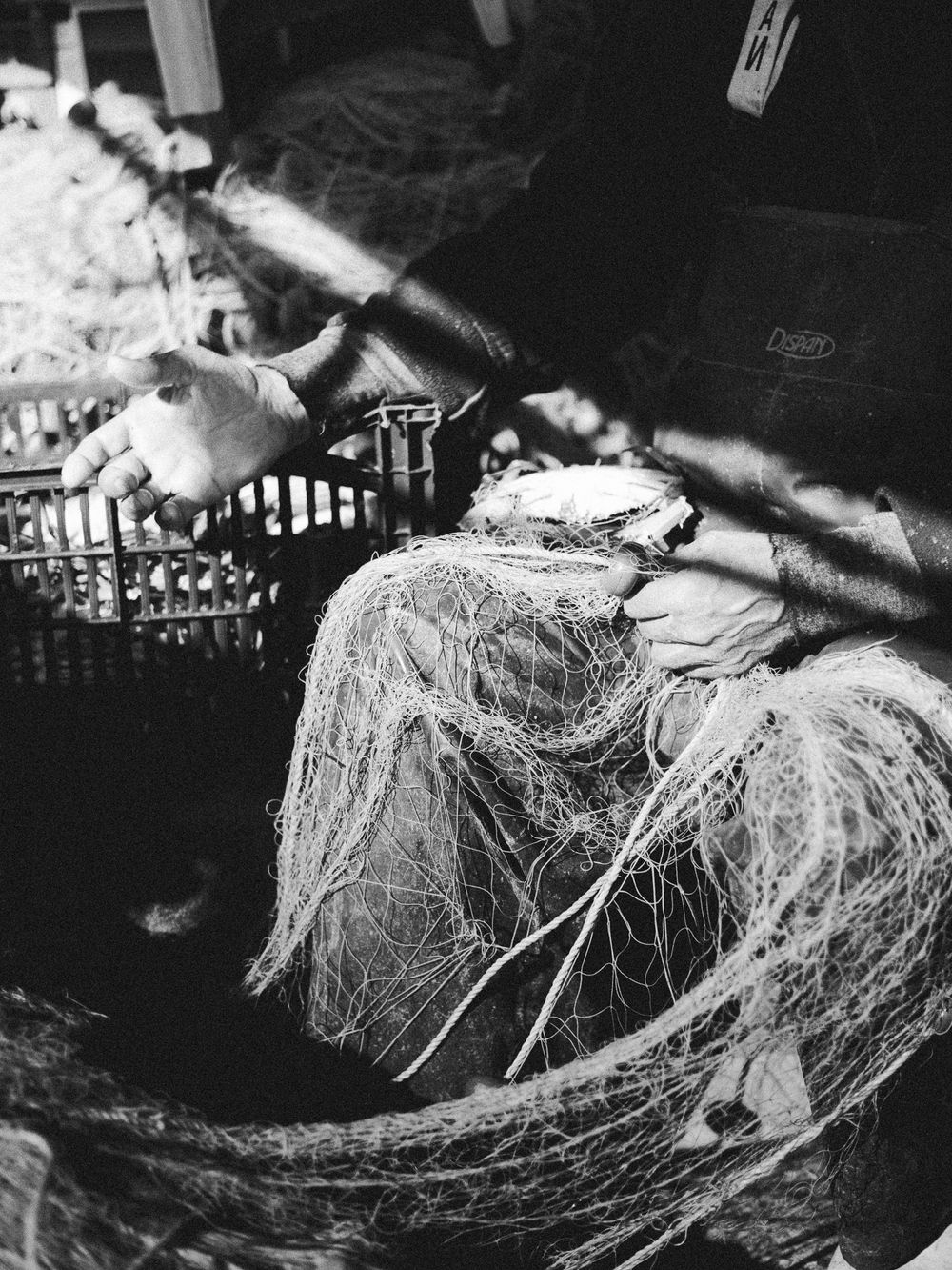 Close-up of tangled fishing nets and hands at work on a traditional Greek fishing boat, black and white documentary photography.
