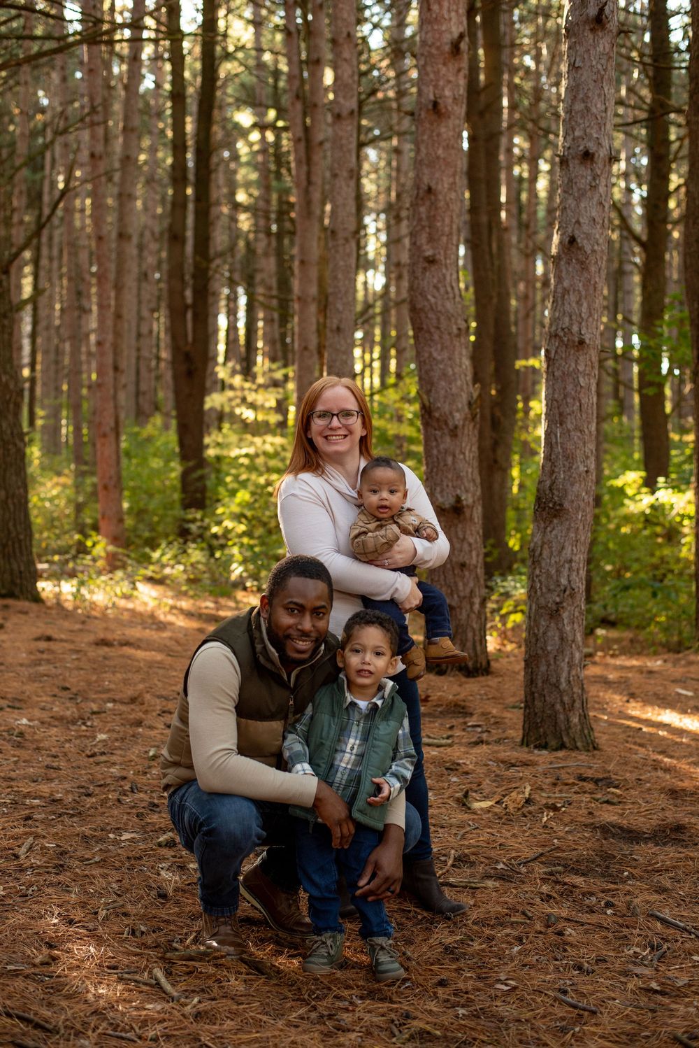 A family of four taking happy family photos in front of tall pine trees in Grand Rapids, Michigan