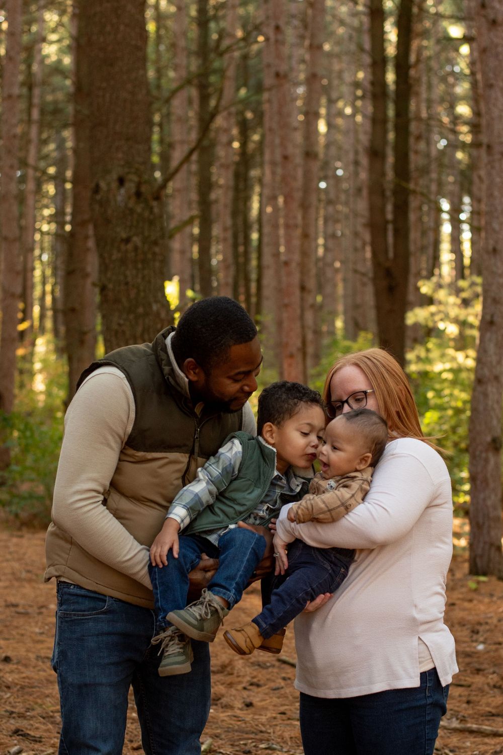 A family of four, kissing each other in a forrest of tall pine trees in Grand Rapids, Michigan