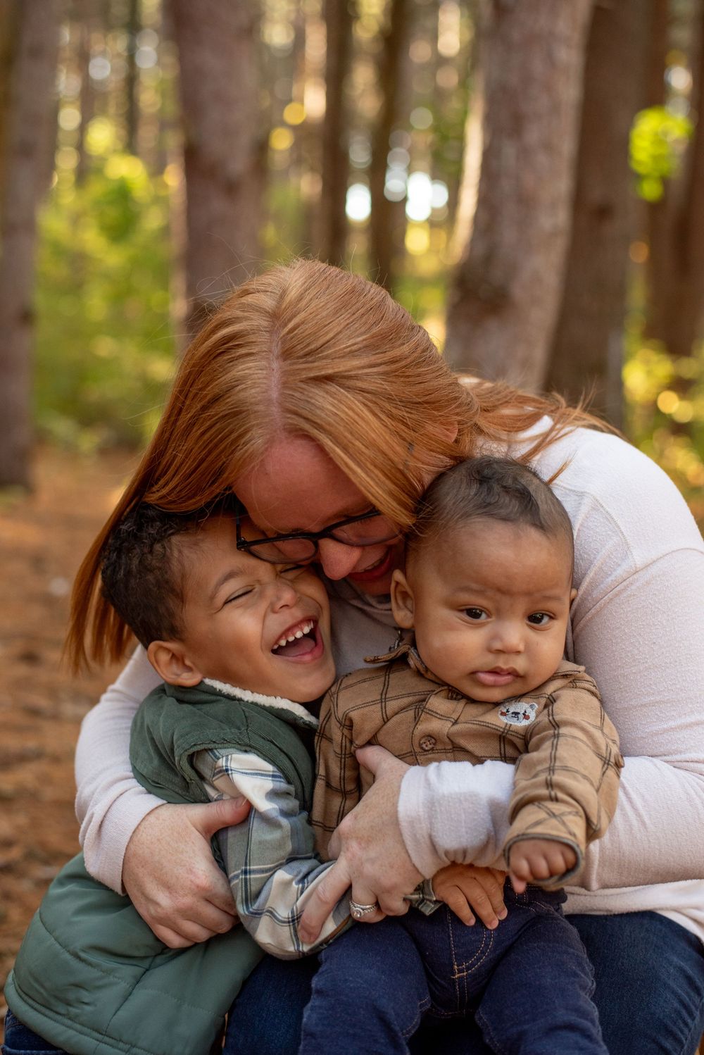 A mom hugging her laughing sons in front of tall pine trees in Grand Rapids, Michigan