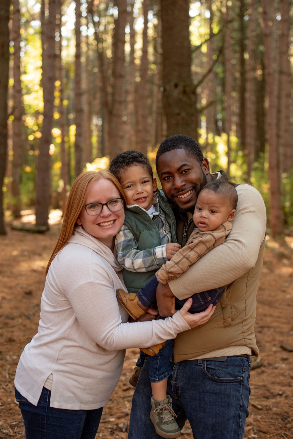 A family hugging each other closely and smiling in a forrest of tall pine trees in Grand Rapids, Michigan