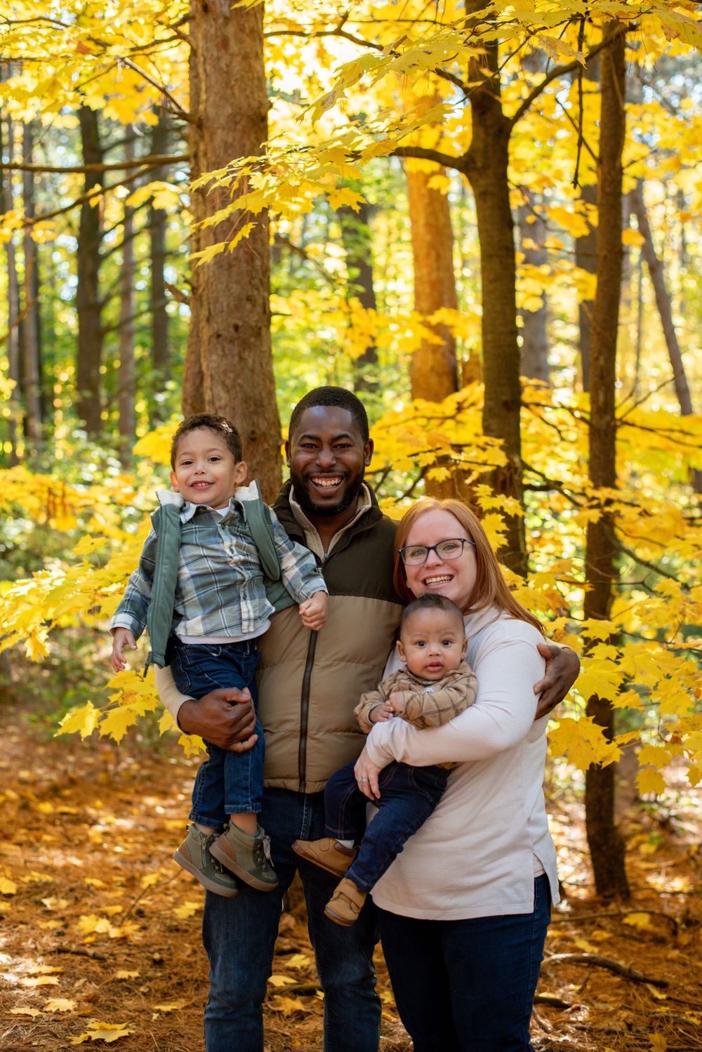 A family standing in front of fall trees, happily smiling in Grand Rapids, Michigan
