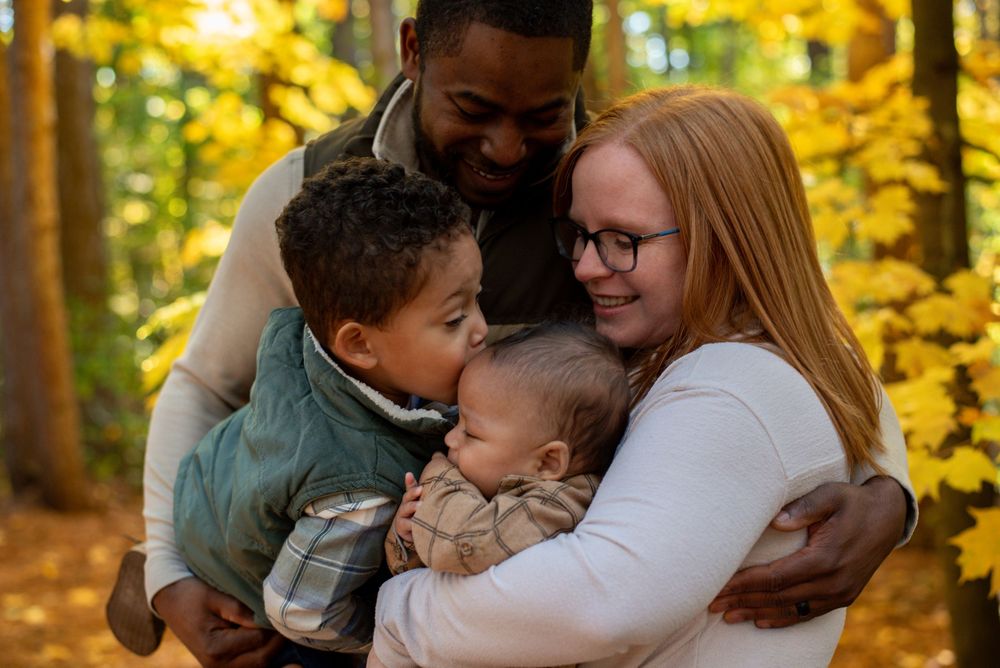 A mom and dad hugging, holding their sons in front of yellow autumn trees in Grand Rapids, Michigan