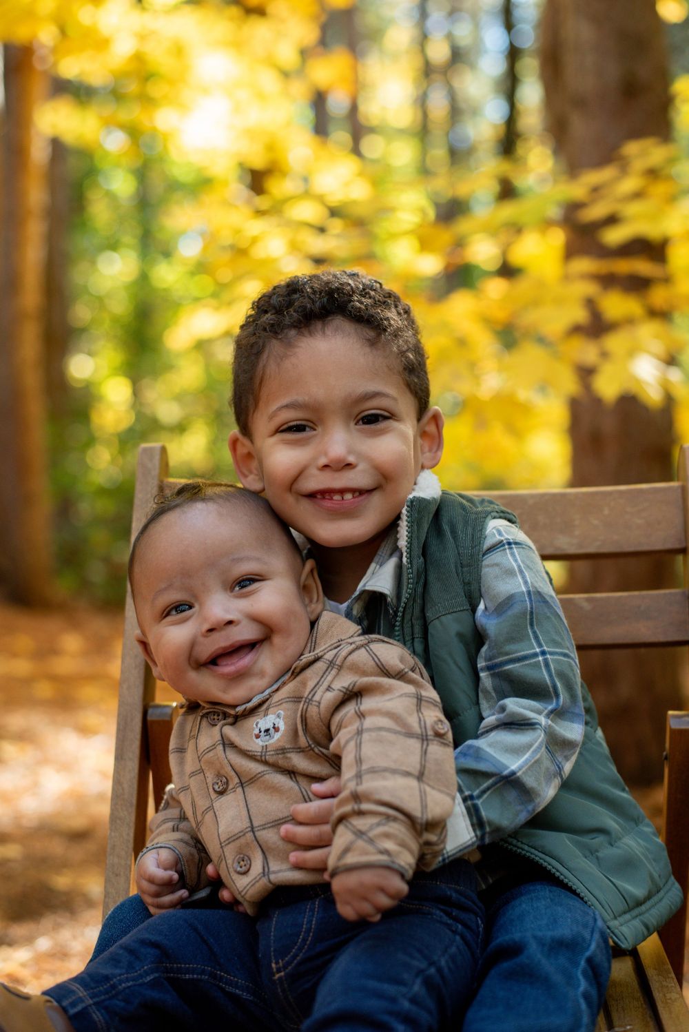 A older brother holding his baby brother in front of yellow fall trees in Grand Rapids, Michigan