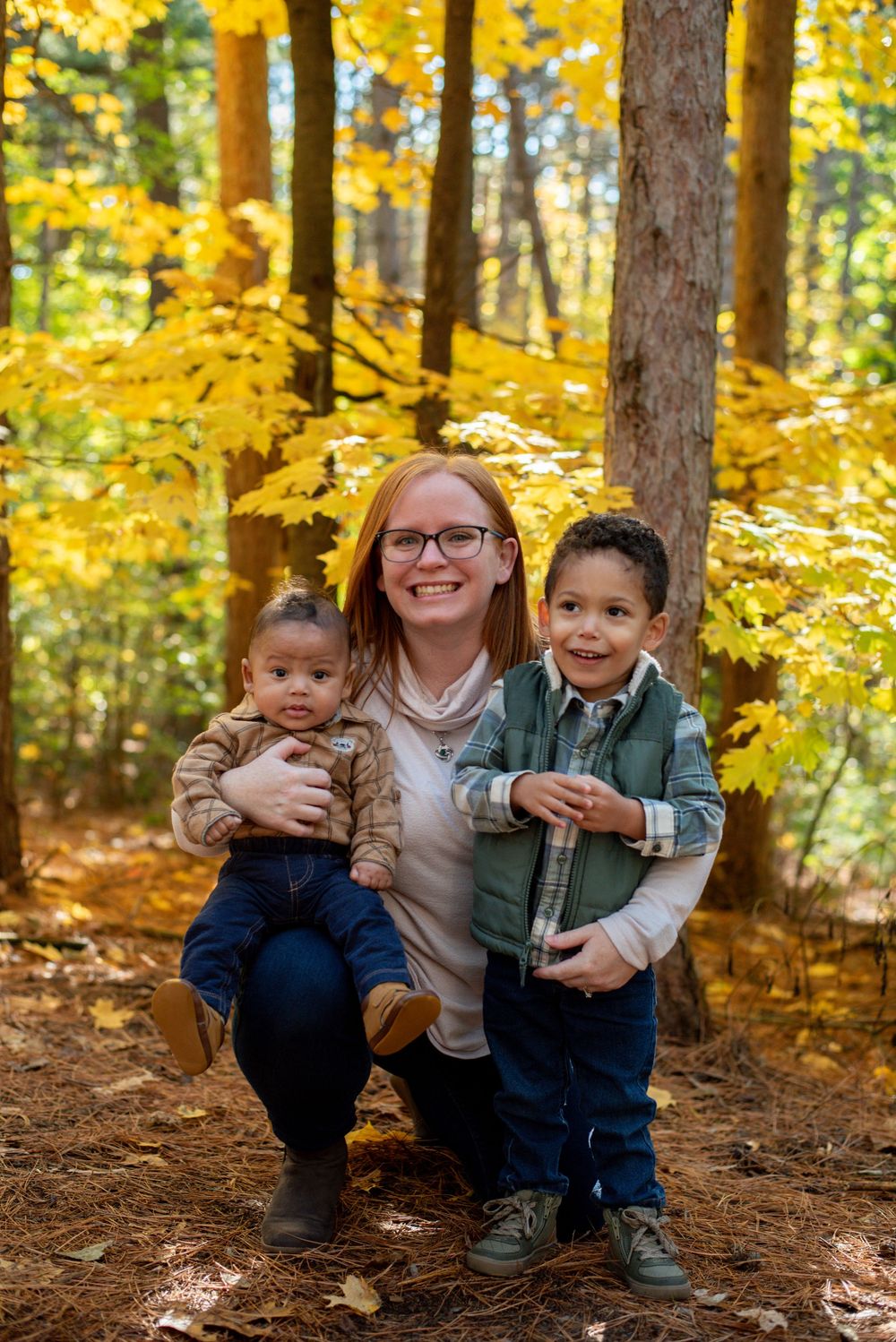 A mom holding her baby and toddler and happily smiling in fall in Grand Rapids, Michigan