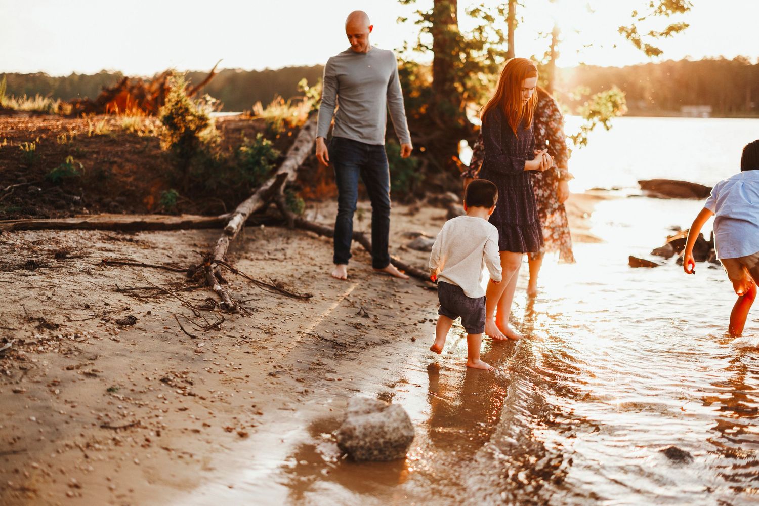 A family plays together at the beach during golden hour sunset, splashing in the shallow water.