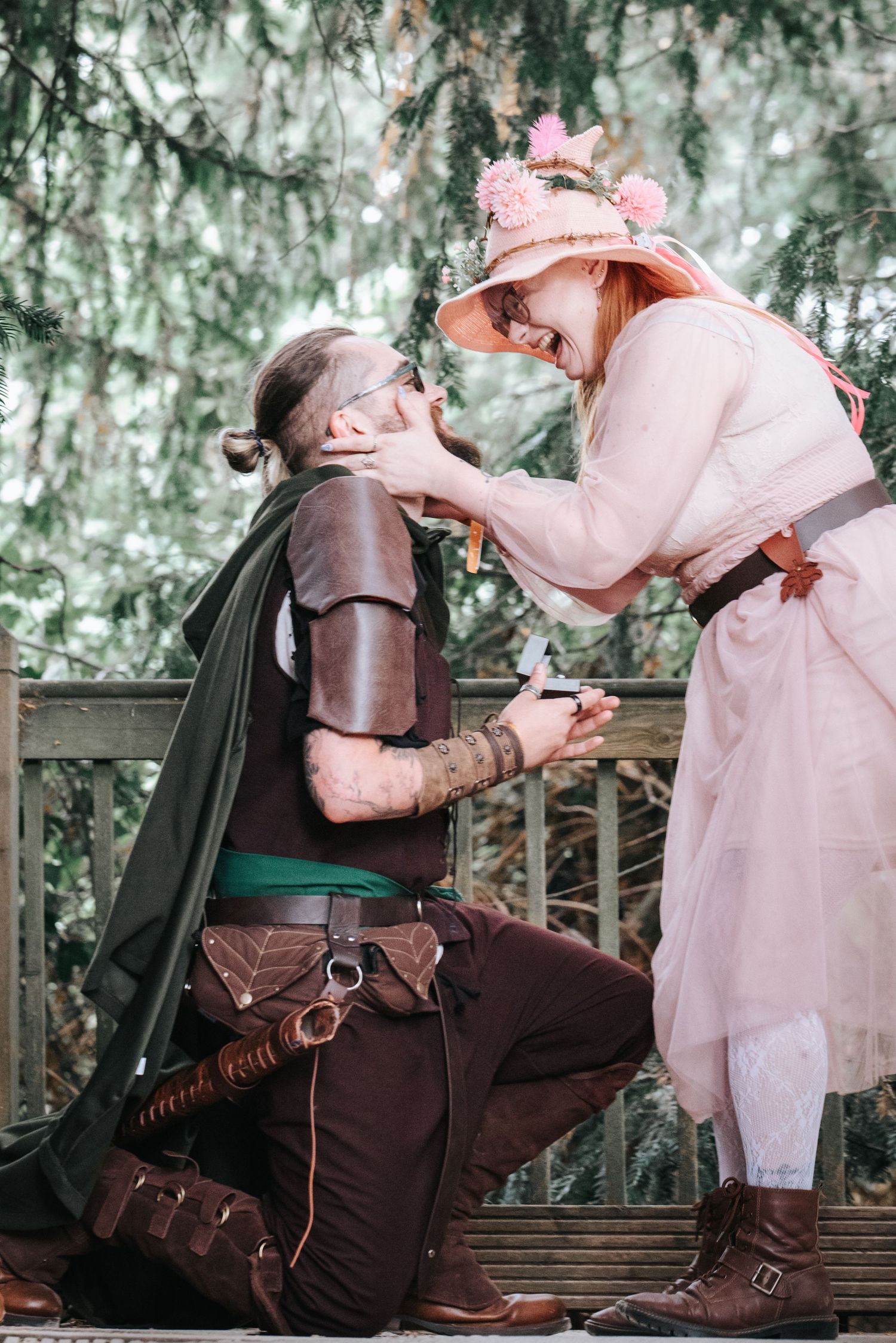 A fantasy-themed couple in medieval and princess costumes share a romantic moment on a bench.