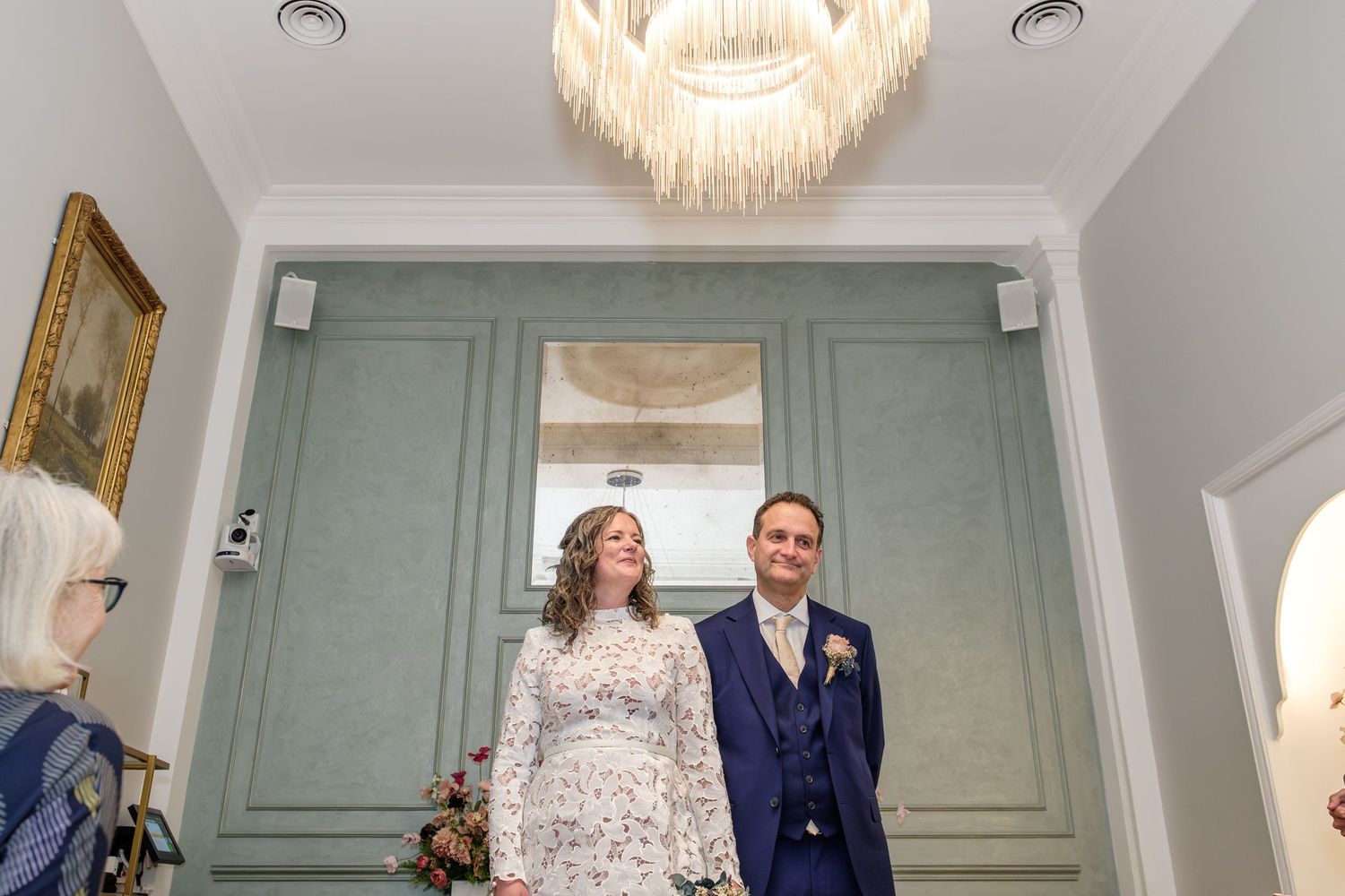 Elegant wedding venue with crystal chandelier and sage green paneled walls.