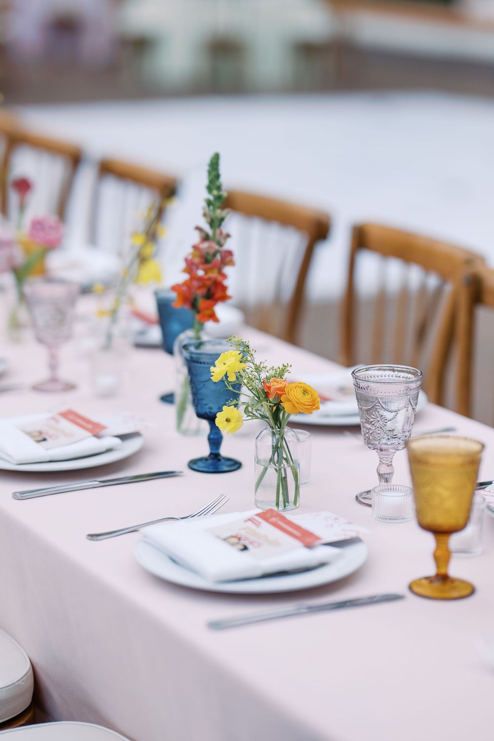 Elegant table settings with white linens, colorful flower centerpieces, and amber glassware at a formal dining event.